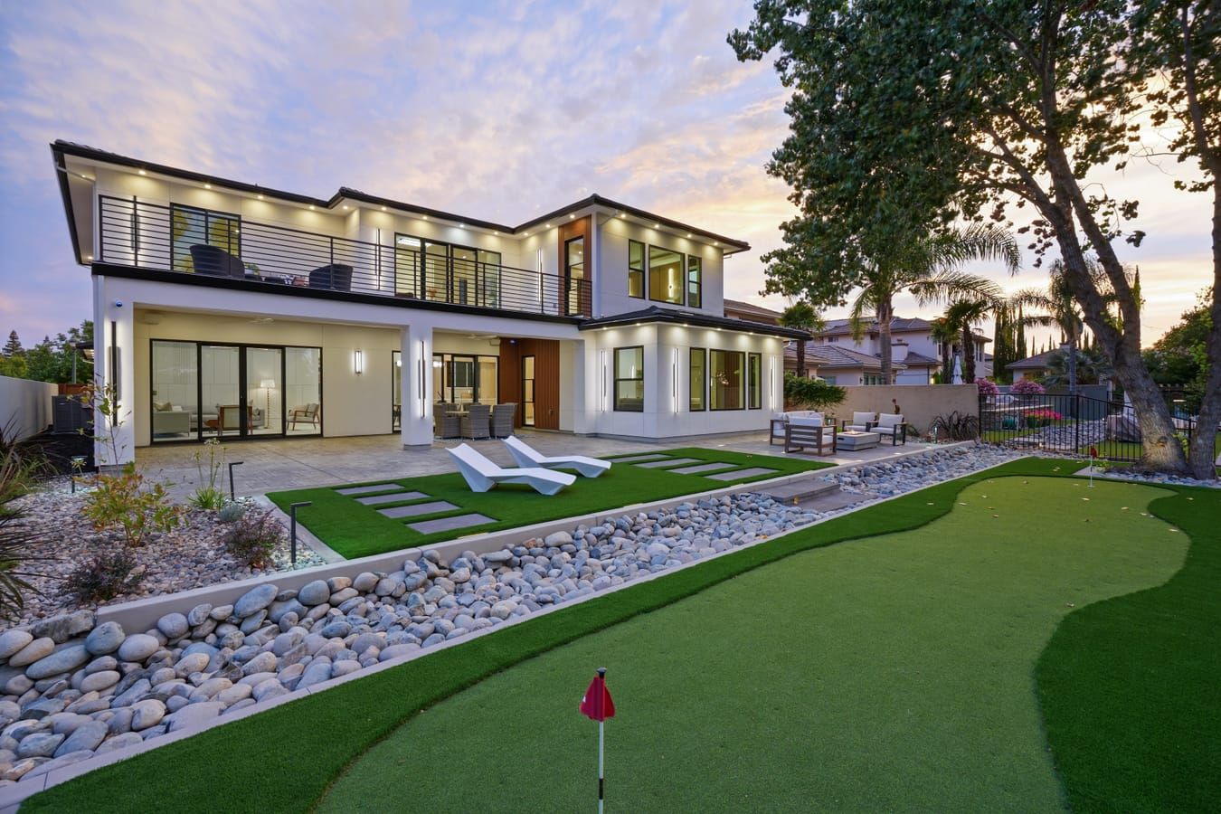 Rear of the home at twilight with terraced landscaping and putting green